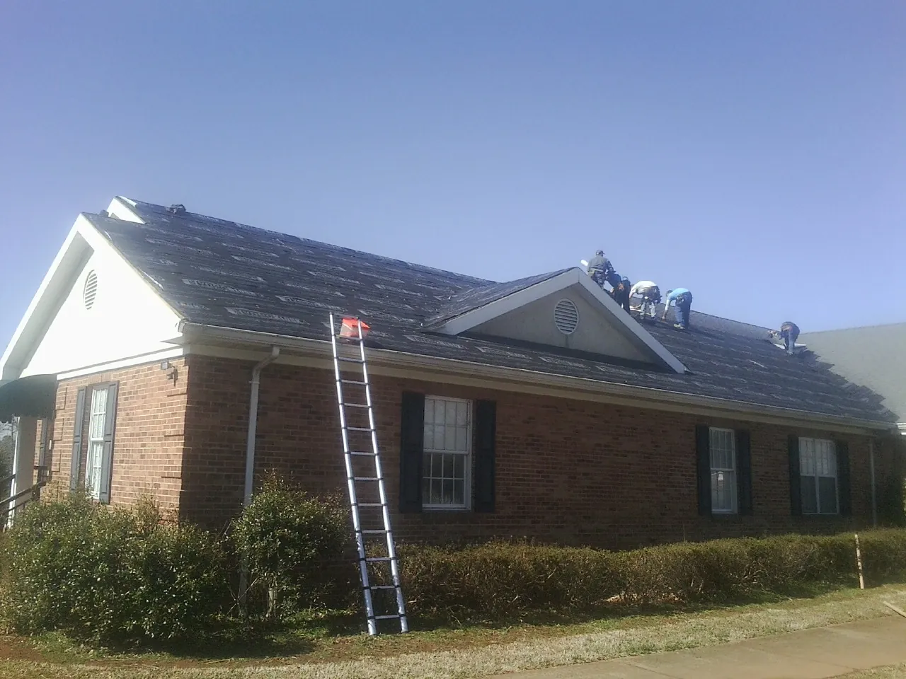 Crew tearing shingles off a brick ranch roof with a ladder set — Emergency Roof Repair work by our crew in Cross Hill