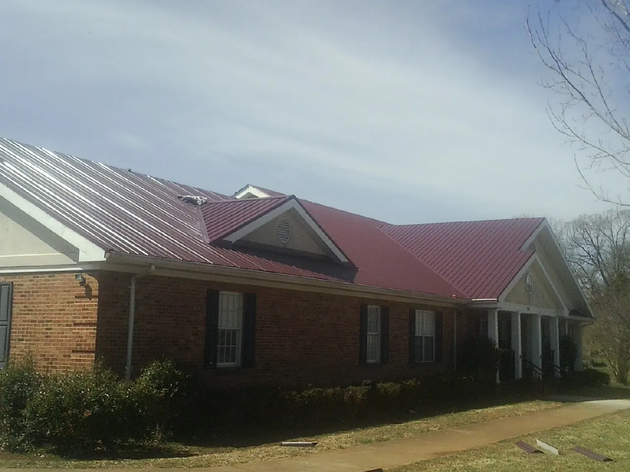 Red metal roof with gabled entries on a long brick building, from a Hail Damage Roof Repair job in Cross Hill