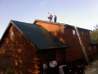 Crew on the ridge of a green metal roof on a two story log home in Cross Hill