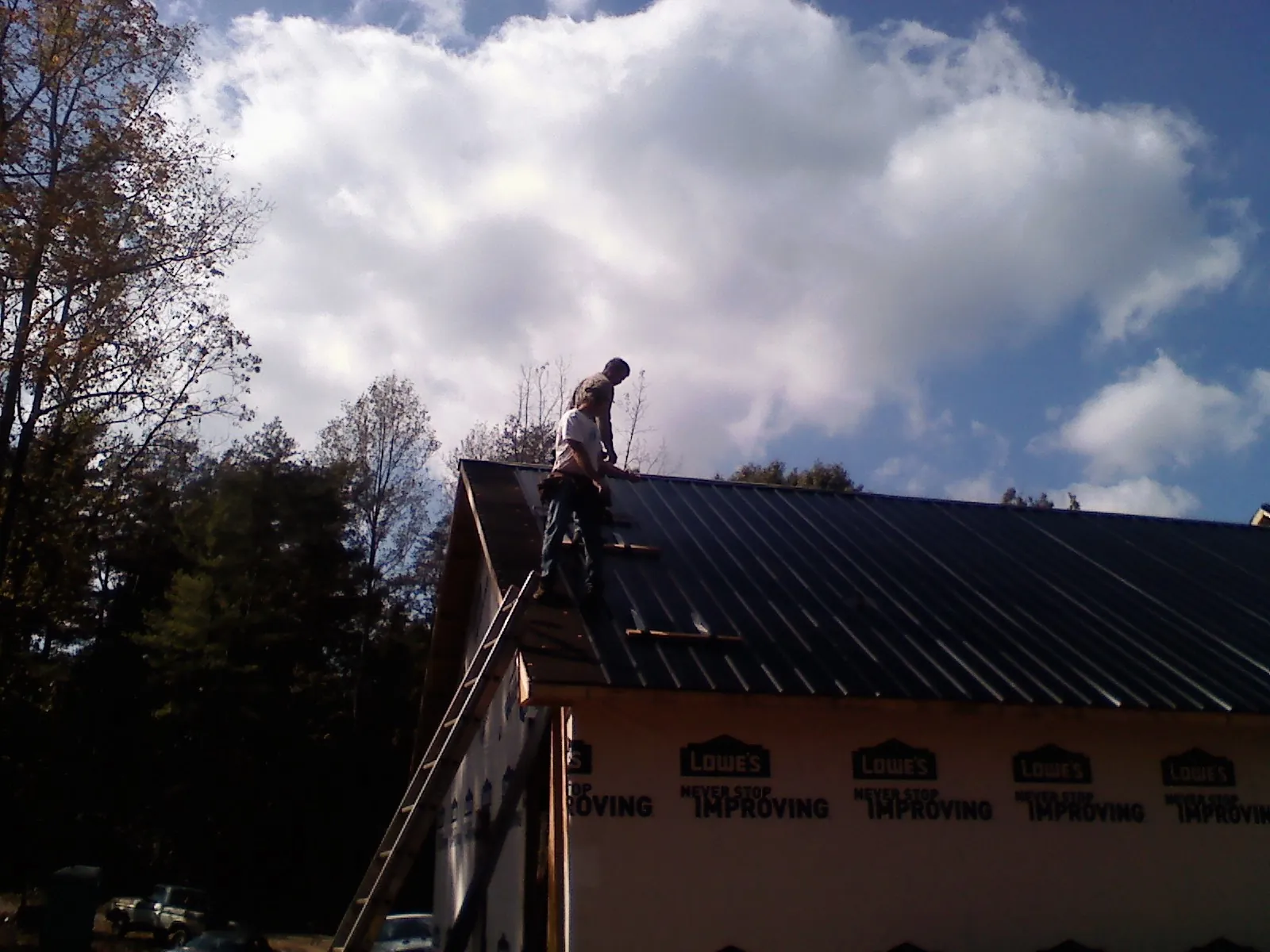 Roofer fastening dark metal panels high against a cloudy sky, from a Roof Inspection job in Cross Hill