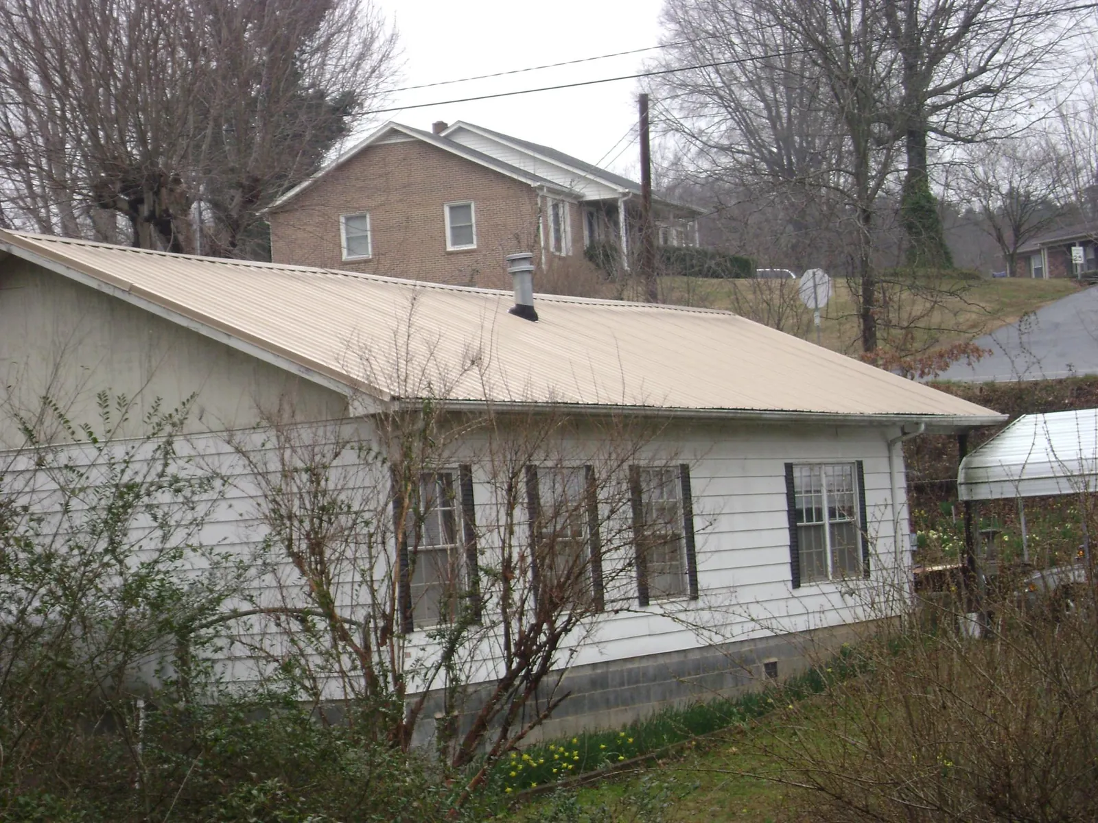 Tan metal roof on a white sided house set into a hillside — Commercial Roofing by Roofing Brothers in Cross Hill