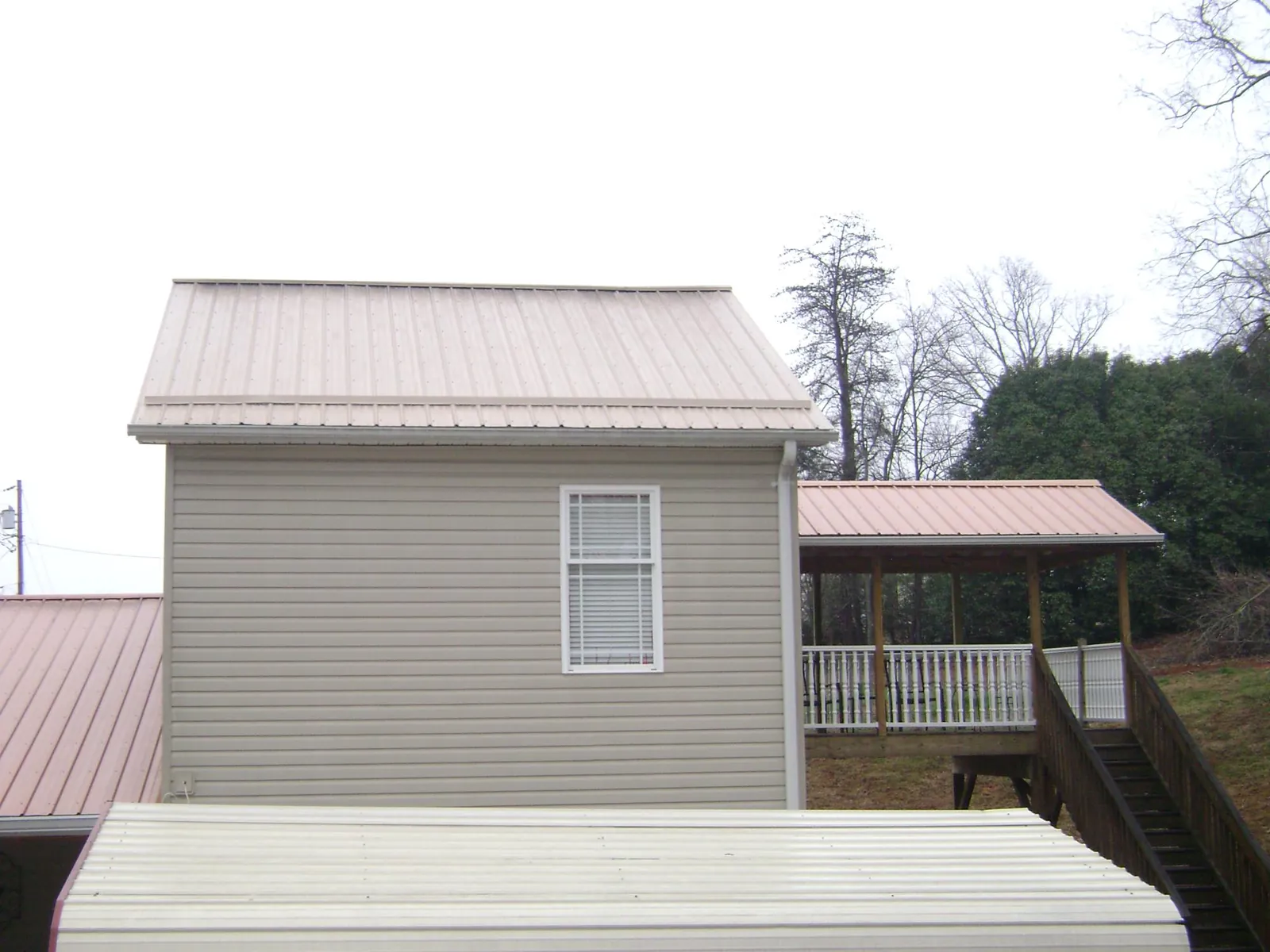 Tan metal roofs on a two story addition and attached porch, from a Roof Replacement job in Cross Hill